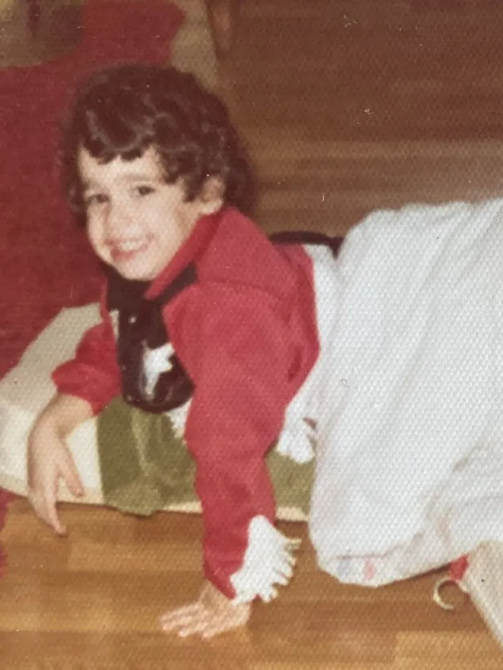 Franco Zuccoli as a small boy, smiling over his shoulder on a wooden floor, a blanket over his legs