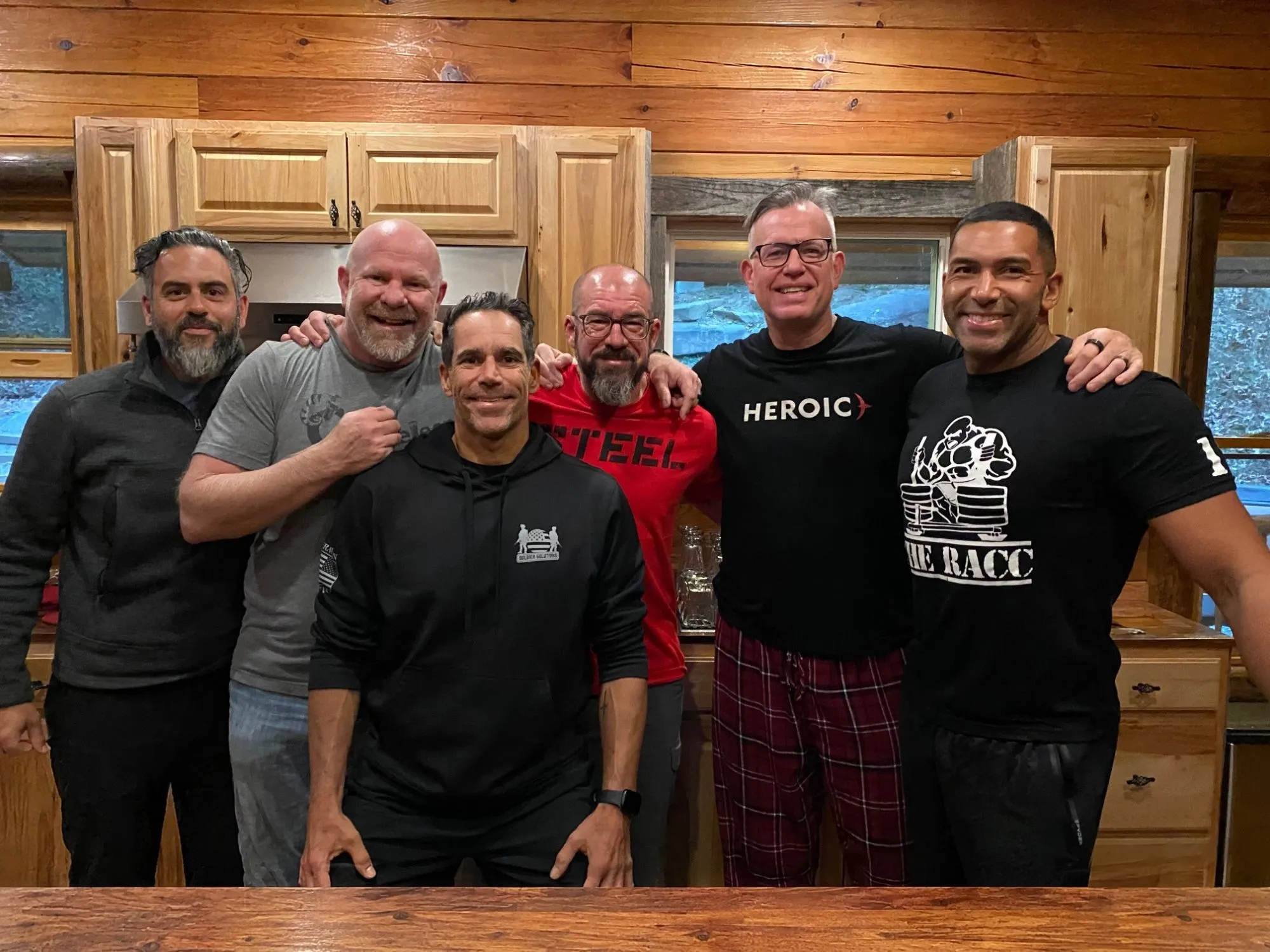 Franco Zuccoli with a group of men in a cabin kitchen, arms around each other, all smiling